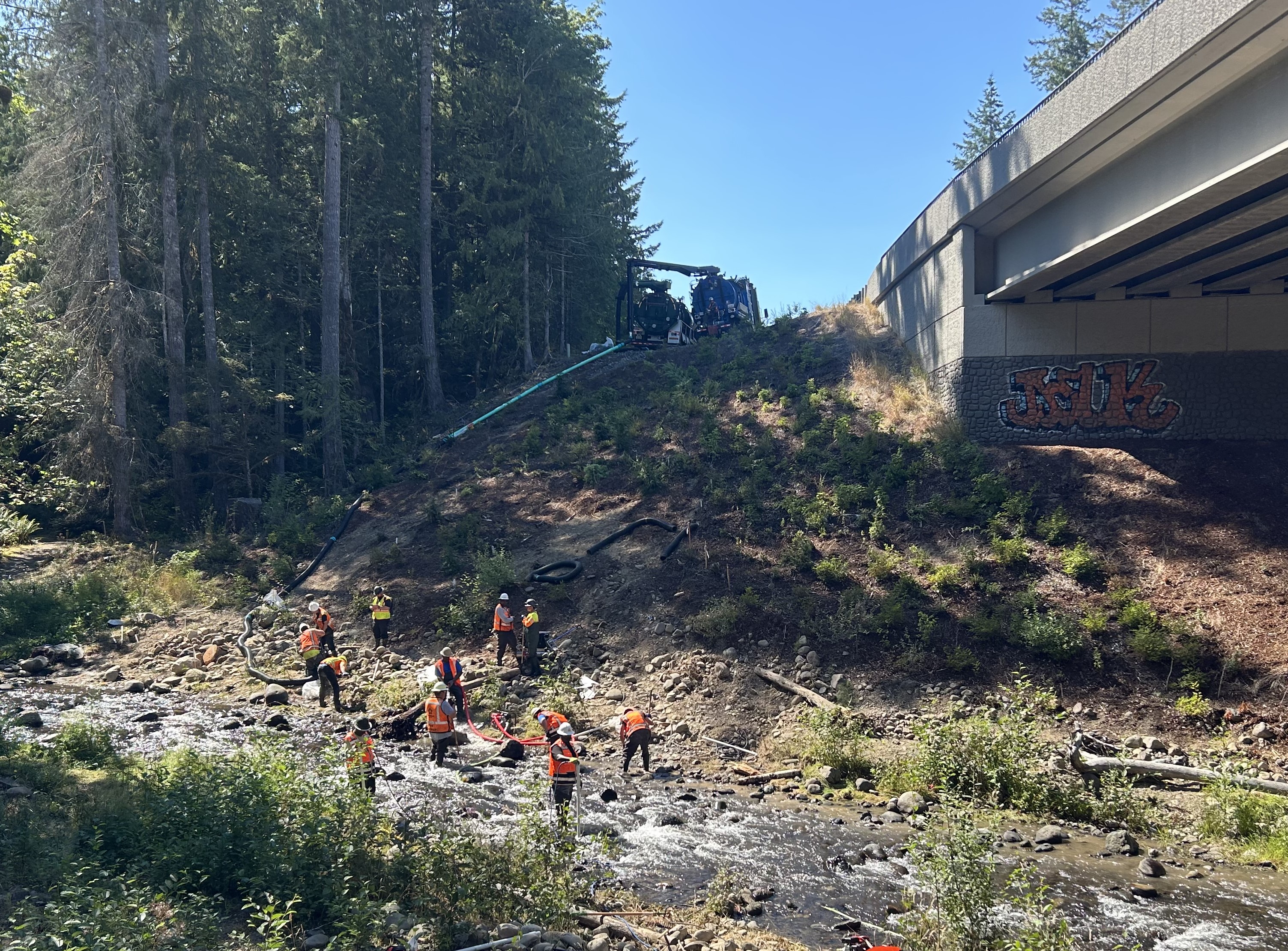 Crews work in Indian Creek near bridge, using a vac truck to remove fuel.
